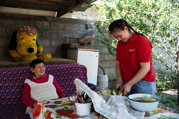 Die 64-jährige Aitbubu Soltonalieva lacht und plaudert, während Ayana Kadyrova das Mittagessen zubereitet. Die erst 16-jährige Freiwillige vom Kirgisischen Roten Halbmond schenkt der alleinstehenden Frau lebensnotwendige Zuwendung. (Foto: Danil Usmanov/SRK/Fairpicture)